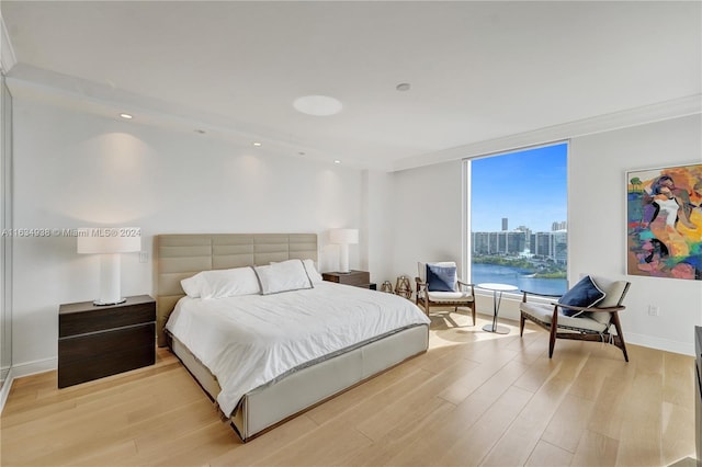 bedroom featuring light hardwood / wood-style flooring, a water view, and crown molding