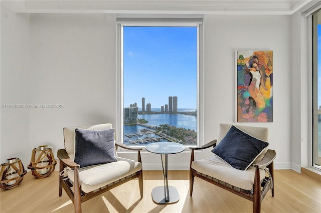 sitting room with ornamental molding, a water view, and light hardwood / wood-style floors