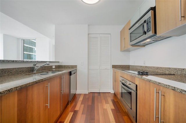 kitchen with appliances with stainless steel finishes, hardwood / wood-style floors, sink, and stone countertops