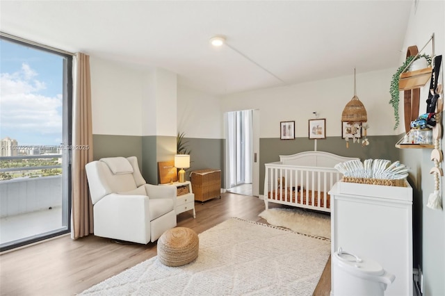 bedroom with floor to ceiling windows, hardwood / wood-style flooring, a crib, and multiple windows