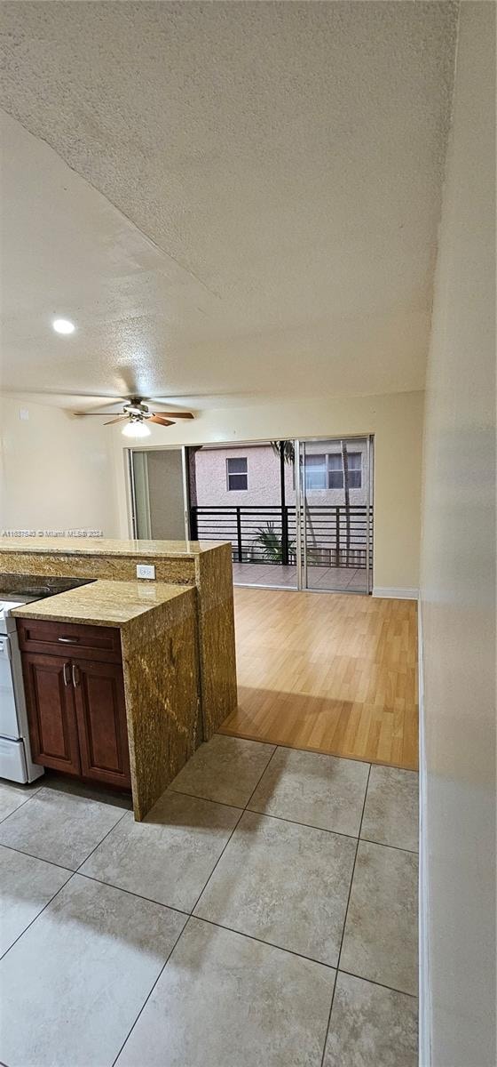 kitchen with a textured ceiling, light hardwood / wood-style flooring, light stone countertops, and ceiling fan