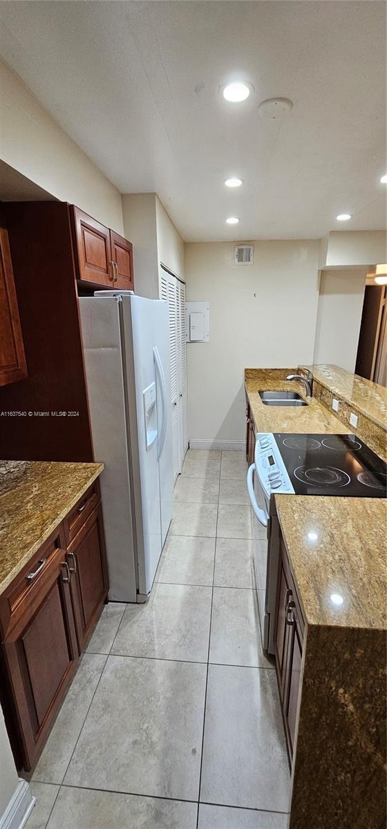 kitchen with range, light tile patterned flooring, light stone counters, white refrigerator with ice dispenser, and sink