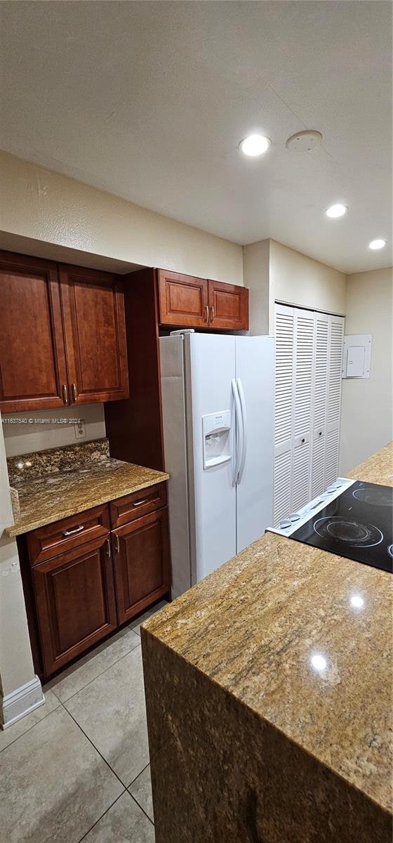 kitchen featuring light tile patterned flooring, stone countertops, stove, and white refrigerator with ice dispenser