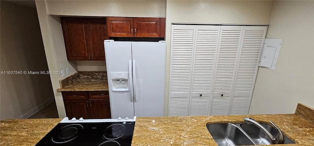 kitchen with white fridge with ice dispenser, light stone counters, a sink, and black electric cooktop