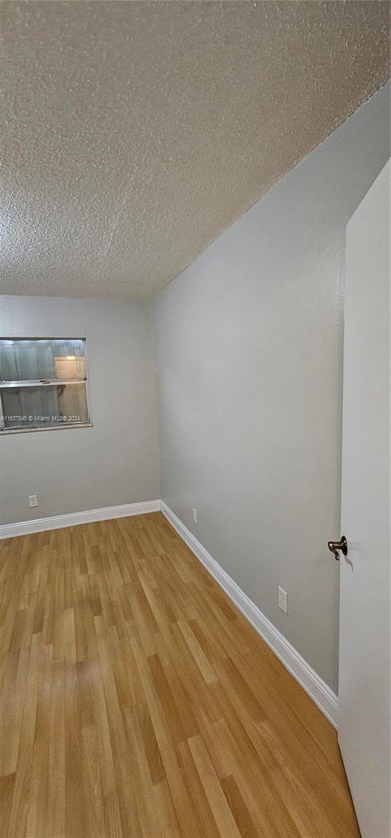 empty room with a textured ceiling, baseboards, and wood finished floors