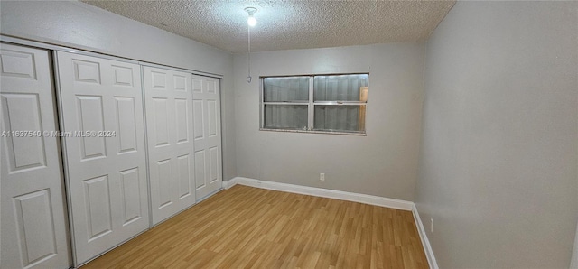 unfurnished bedroom with light wood-type flooring, a closet, a textured ceiling, and baseboards