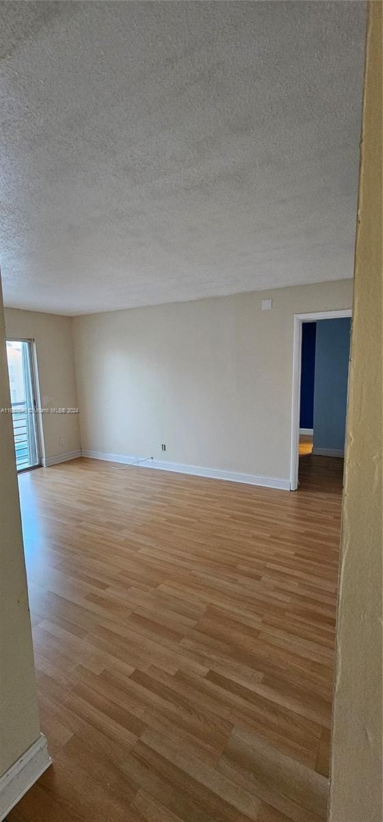 unfurnished room with a textured ceiling, light wood-type flooring, and baseboards