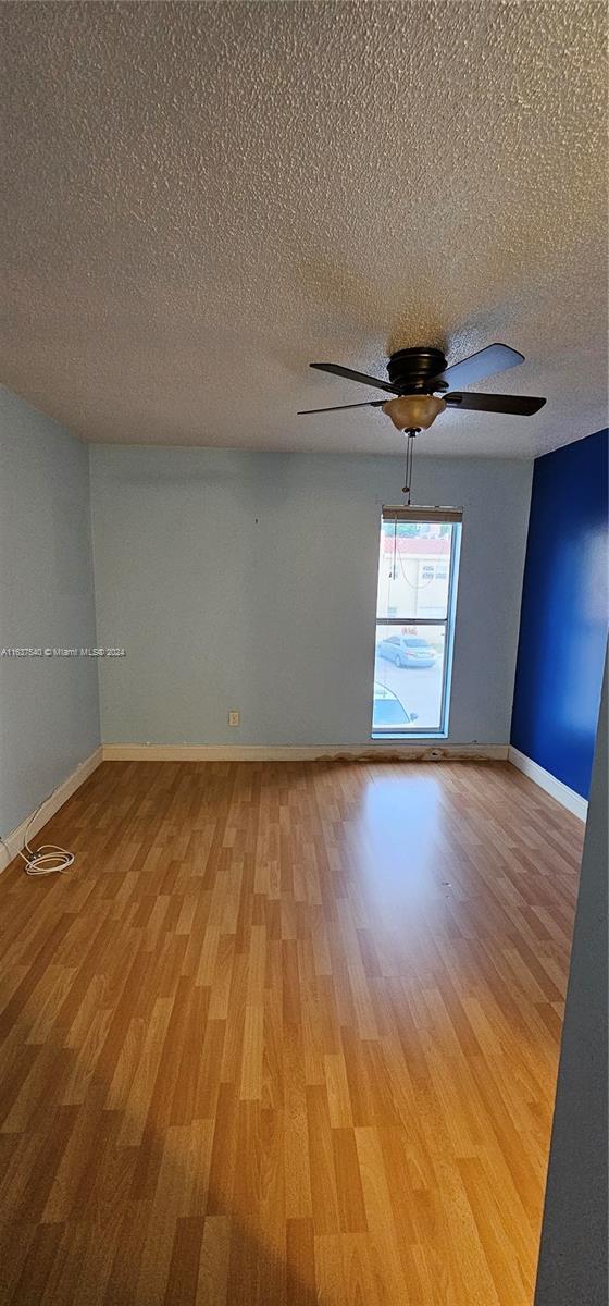 empty room with ceiling fan, light wood-style flooring, baseboards, and a textured ceiling