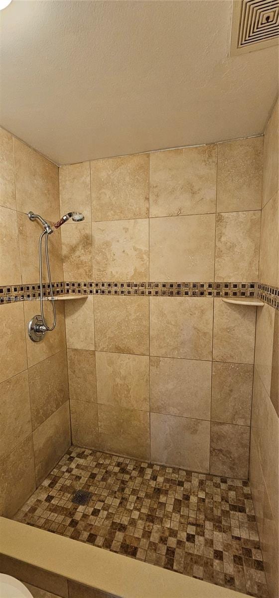 full bath with visible vents, a tile shower, and a textured ceiling