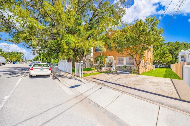 view of property hidden behind natural elements featuring uncovered parking, stone siding, and fence