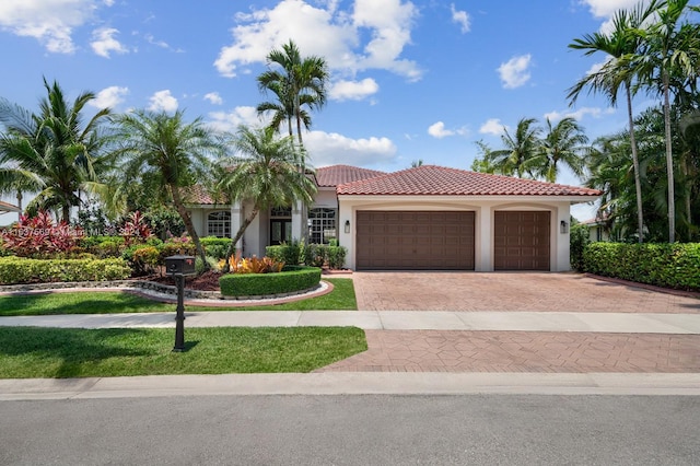 mediterranean / spanish house with a garage, decorative driveway, a tiled roof, and stucco siding