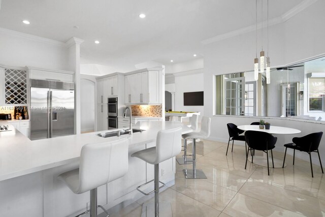 kitchen featuring stainless steel appliances, white cabinets, hanging light fixtures, backsplash, and a kitchen breakfast bar