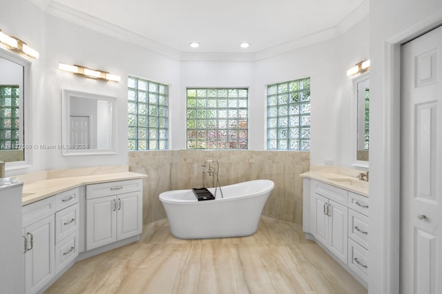 full bath with plenty of natural light, ornamental molding, a soaking tub, and two vanities