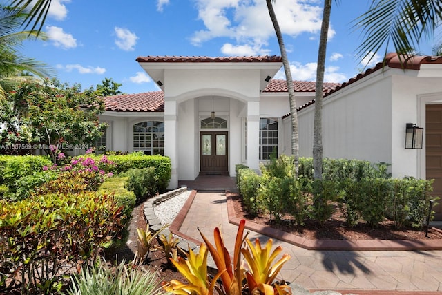 view of exterior entry featuring a garage, a tile roof, and stucco siding