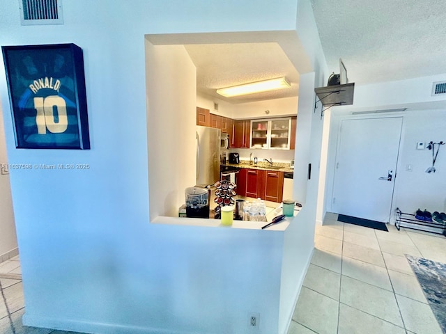 3300 NE 191st St Unit 515, Aventura, FL 33180 - kitchen featuring stainless steel appliances, a textured ceiling, light tile patterned floors, light countertops, and glass insert cabinets