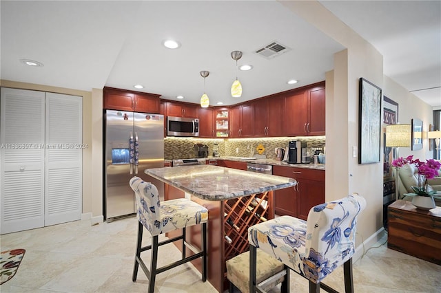 kitchen with light stone counters, tasteful backsplash, decorative light fixtures, a kitchen breakfast bar, and appliances with stainless steel finishes