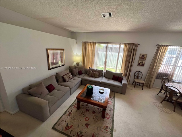 living area featuring a textured ceiling, visible vents, light carpet, and a healthy amount of sunlight