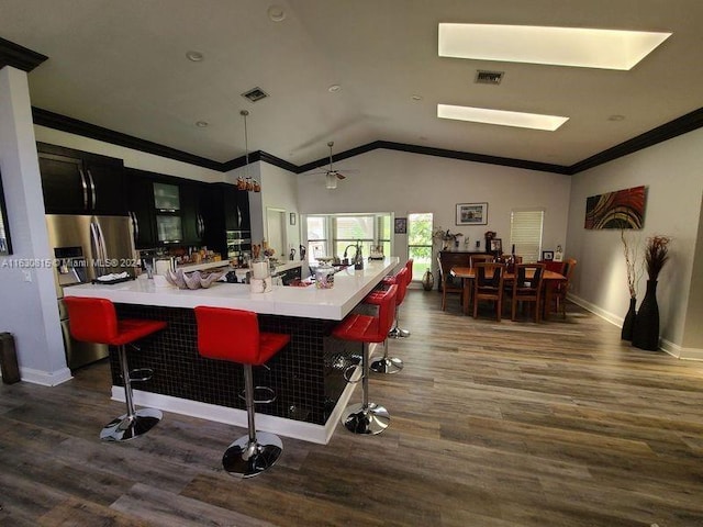 kitchen featuring crown molding, vaulted ceiling, wood-type flooring, and a kitchen breakfast bar