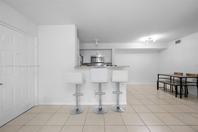 kitchen with white cabinetry, a kitchen breakfast bar, a textured ceiling, light tile patterned floors, and kitchen peninsula