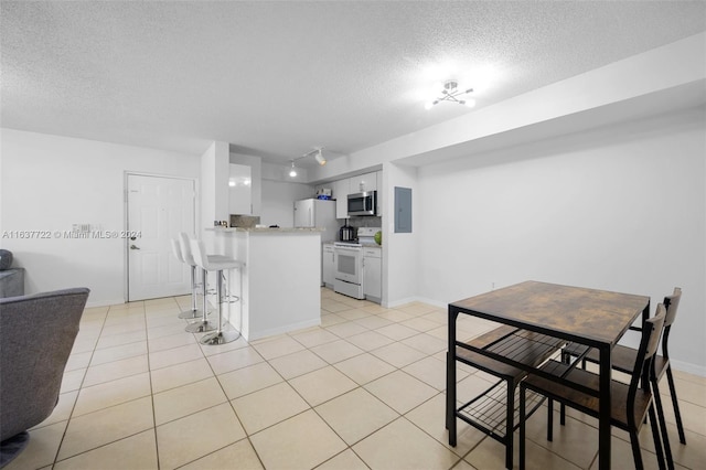 kitchen with a kitchen bar, a textured ceiling, white cabinets, white appliances, and light tile patterned flooring