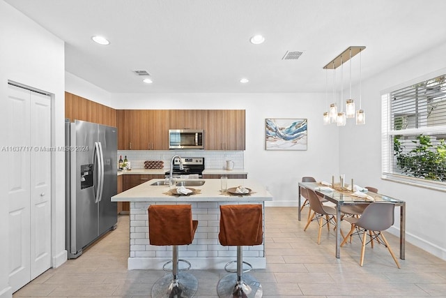 kitchen featuring hanging light fixtures, an island with sink, appliances with stainless steel finishes, a breakfast bar area, and sink