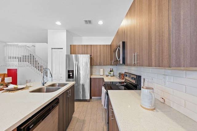 kitchen featuring backsplash, light stone countertops, light hardwood / wood-style flooring, sink, and stainless steel appliances