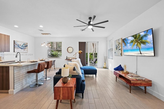 living room featuring sink, light wood-type flooring, and ceiling fan with notable chandelier