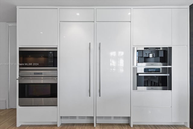 kitchen featuring stainless steel double oven, light hardwood / wood-style floors, and white cabinetry