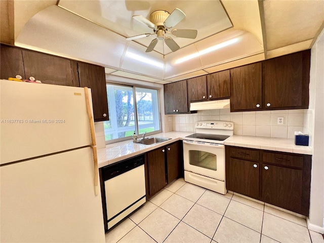 kitchen with dark brown cabinetry, decorative backsplash, white appliances, a tray ceiling, and ceiling fan