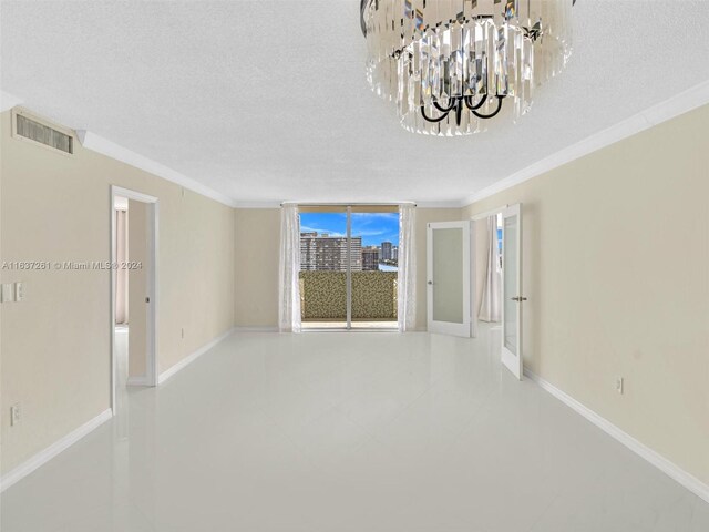 tiled spare room with crown molding, a textured ceiling, and a notable chandelier