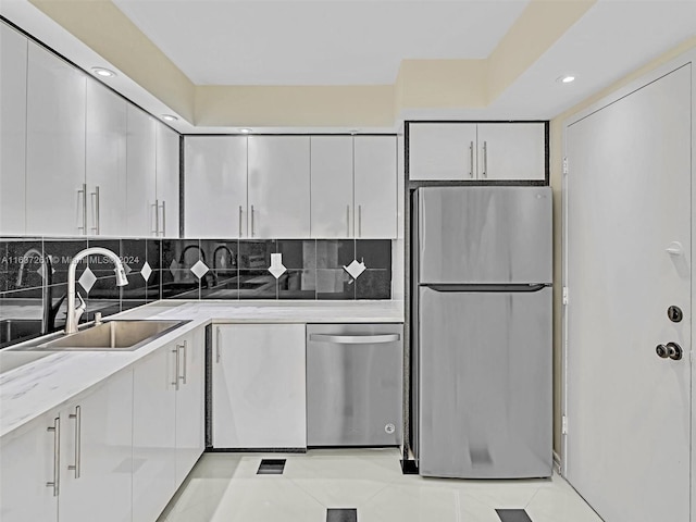 kitchen featuring white cabinets, stainless steel appliances, sink, backsplash, and light tile patterned floors