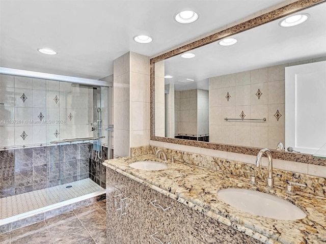 bathroom with dual vanity, a shower with shower door, tile patterned flooring, and tile walls