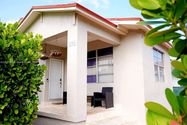 view of exterior entry with covered porch and stucco siding