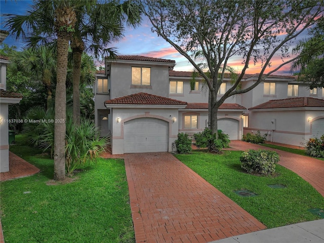 mediterranean / spanish-style home featuring decorative driveway, a tile roof, stucco siding, a front lawn, and a garage