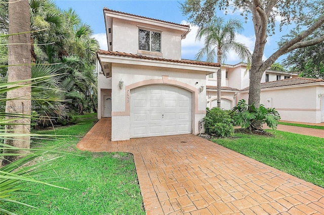 mediterranean / spanish house featuring stucco siding, decorative driveway, a tiled roof, a front lawn, and an attached garage