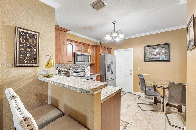 kitchen featuring stainless steel appliances, a chandelier, a textured wall, a peninsula, and crown molding