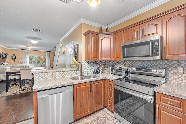 kitchen with stainless steel appliances, a sink, open floor plan, crown molding, and light stone counters