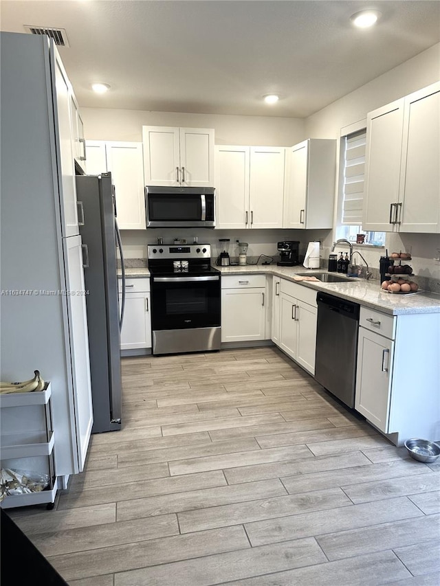 kitchen with appliances with stainless steel finishes, light hardwood / wood-style flooring, sink, light stone countertops, and white cabinetry