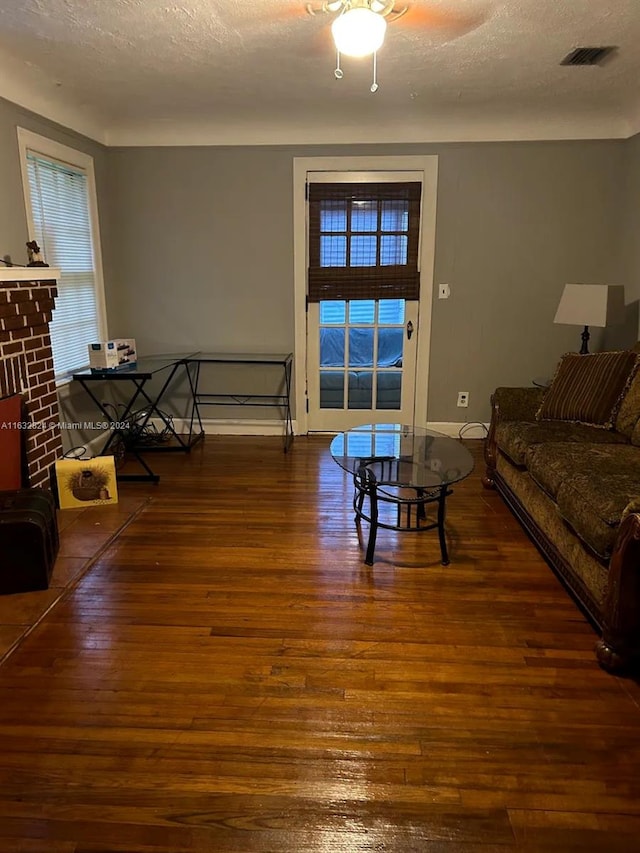 living room with ceiling fan, a brick fireplace, hardwood / wood-style floors, and a textured ceiling