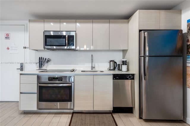 kitchen with appliances with stainless steel finishes, light hardwood / wood-style flooring, white cabinetry, and sink