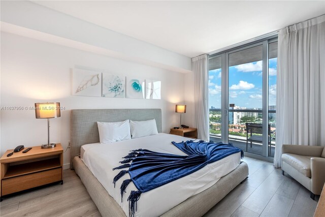 bedroom with light wood-style floors, a city view, floor to ceiling windows, and access to outside