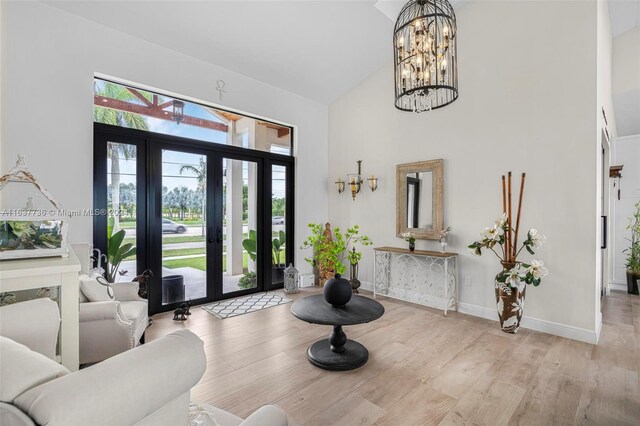 foyer entrance featuring french doors, high vaulted ceiling, light hardwood / wood-style flooring, and a chandelier