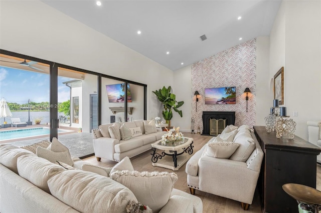 living room featuring high vaulted ceiling, light wood-type flooring, and a tile fireplace