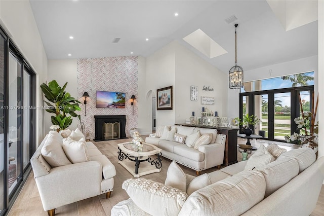 living room featuring a tile fireplace, an inviting chandelier, light wood-type flooring, high vaulted ceiling, and a skylight