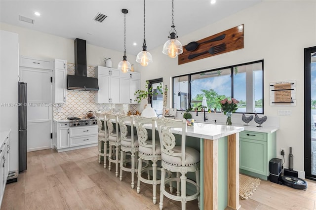 kitchen with a kitchen island, hanging light fixtures, white cabinets, light hardwood / wood-style flooring, and premium range hood