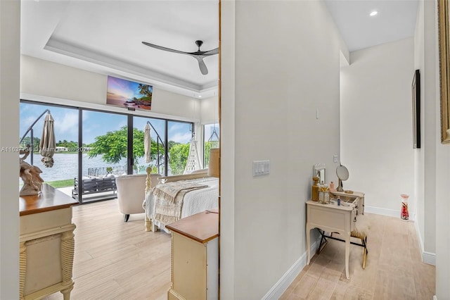 corridor featuring light hardwood / wood-style floors, a tray ceiling, and a water view