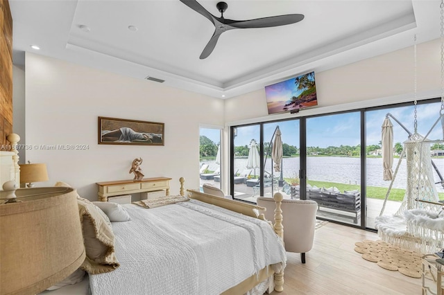 bedroom with access to exterior, a tray ceiling, light wood-type flooring, and ceiling fan