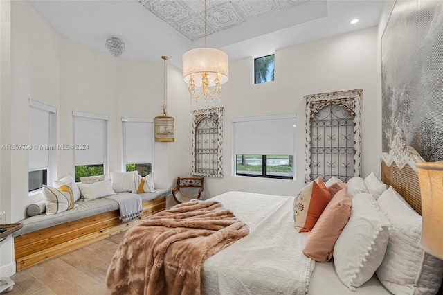 bedroom featuring a chandelier, multiple windows, light wood-type flooring, and a high ceiling