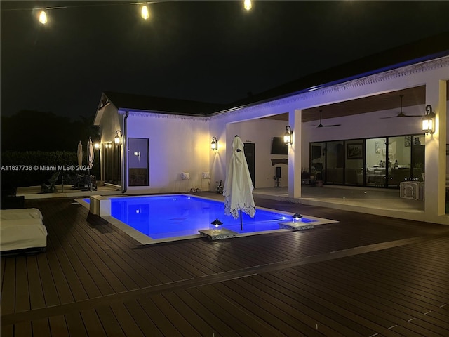 pool at night featuring a patio, ceiling fan, and a deck