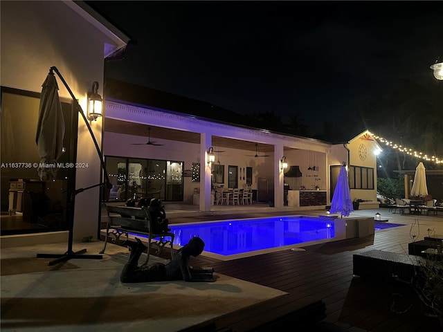 pool at night featuring a deck and ceiling fan